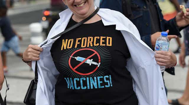 Une femme écarte sa blouse pour montrer son T-shirt "no forced vaccines"