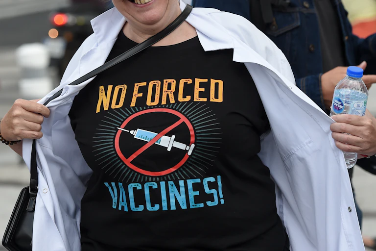 Une femme écarte sa blouse pour montrer son T-shirt "no forced vaccines"