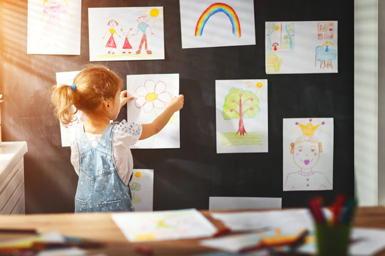 Une petite fille accroche ses dessins au mur