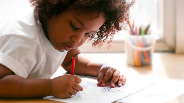 Jeune fille d’âge préscolaire allongée écrivant et dessinant