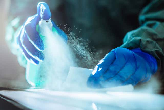 Close-up of gloved hands spraying disinfectant on a wipe and a surface