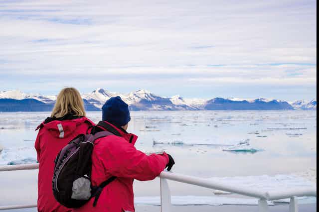 Two ship passengers sailing in Arctic waters looking at melting sea ice floes.