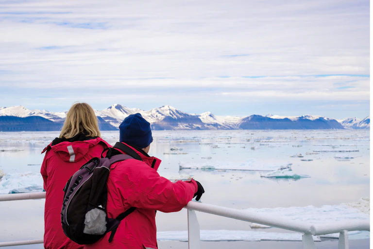 Two ship passengers sailing in Arctic waters looking at melting sea ice floes.