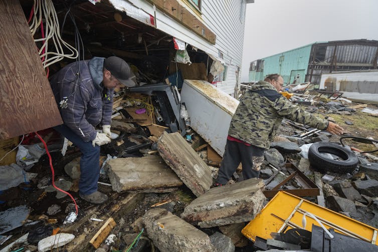 Two men sifting through the rubble of a damaged building.