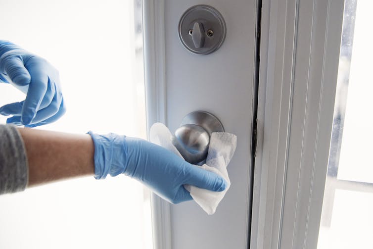Gloved hands wiping doorknob