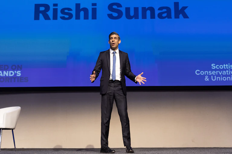 Rishi Sunak giving a speech in front of a huge screen bearing his name.