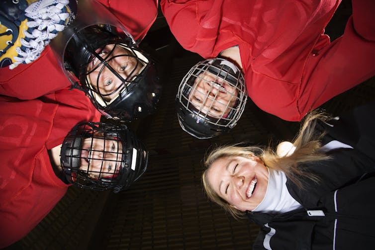 Photo looking up at a huddle of three female hockey players in helmets and gear, and their female coach