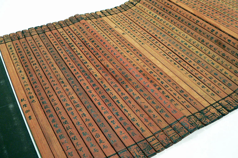 Many thin planks of bamboo tied together to form a book, with Chinese characters written on them.