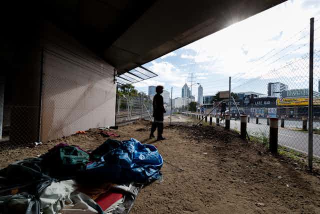 Homeless man sleeping under an overpass looks out across city skyline