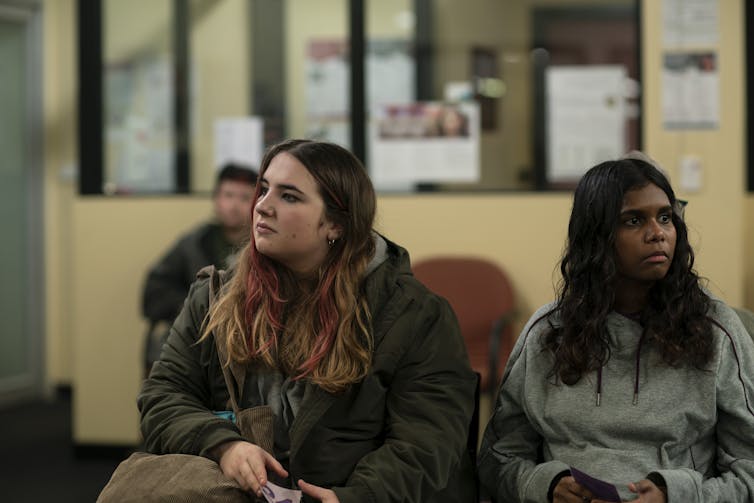 Two young women, one white and one Black, in a waiting room.