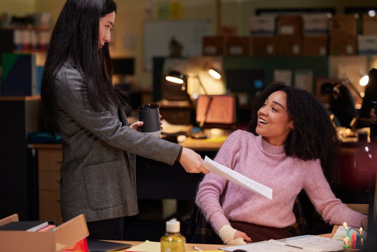 Two women smile at desks.