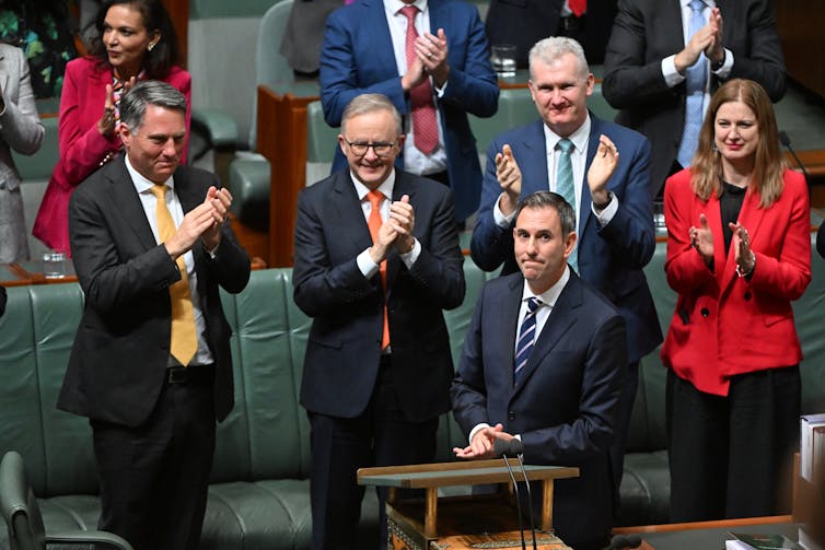 man stands at lectern while others clap