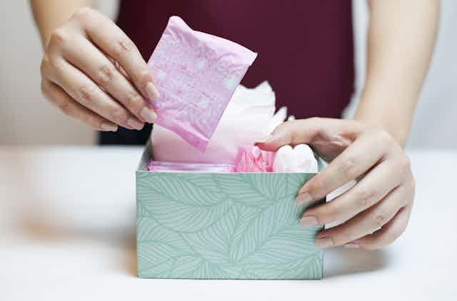 Woman picks up a panty liner from a box of menstrual products