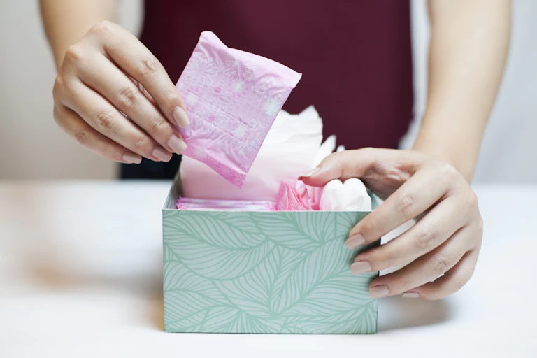 Woman picks up a panty liner from a box of menstrual products