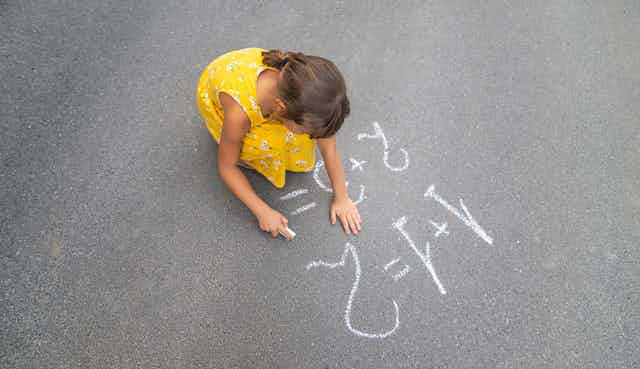 Una niña dibuja sumas en el suelo con una tiza.