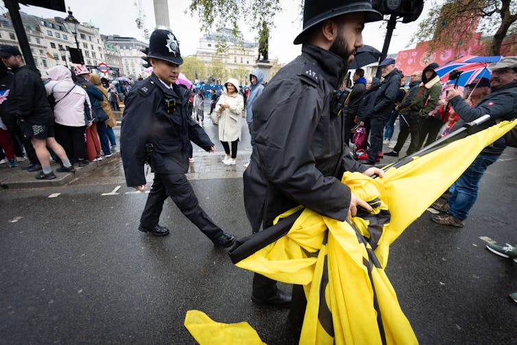 A Met police officer removes a large yellow banner from a Republic anti-monarchy protest.