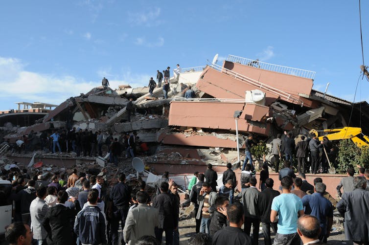Önünde ayakta duran insanlarla depremde yıkılan bir bina.