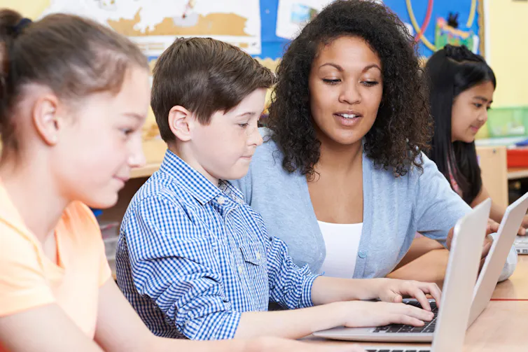 A teacher and two pupils looking at a laptop.