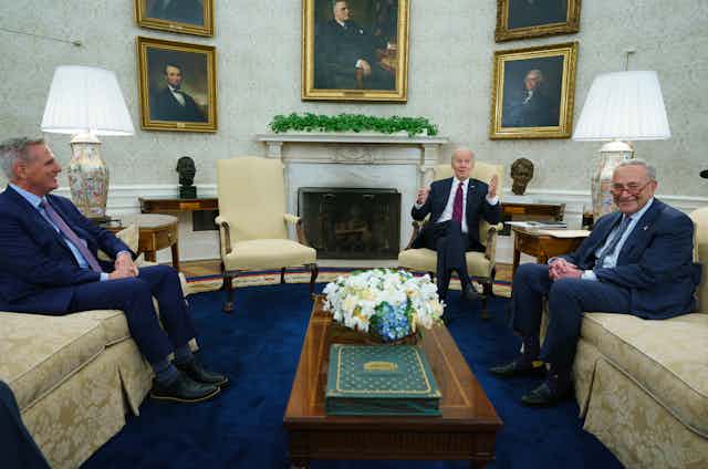 three white men sit on couches and chairs in an ornate room with pictures of past presidents on the wall