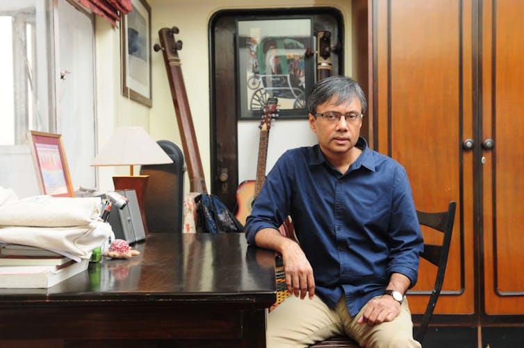 A man sits on a chair in a room with musical instruments.