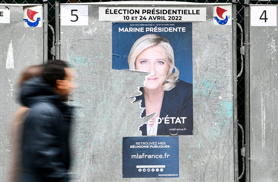 Quelques piétons passent une affiche officielle de campagne de la candidate d'extrême-droite Marine Le Pen (Rassemblement National), sur un panneau d'affichage électoral (enseigne), le 5 avril 2022 à Paris.