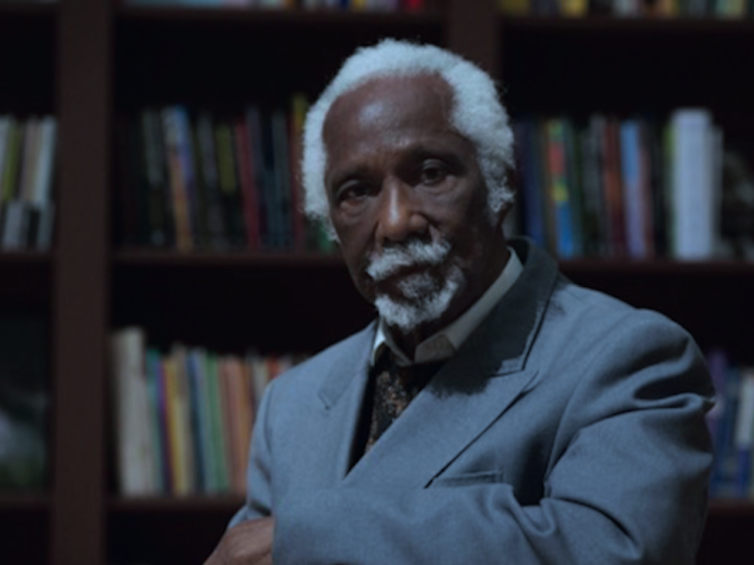 Eric Huntley in a grey jacket, in front of a bookcase.