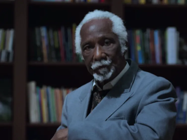 Eric Huntley in a grey jacket, in front of a bookcase.