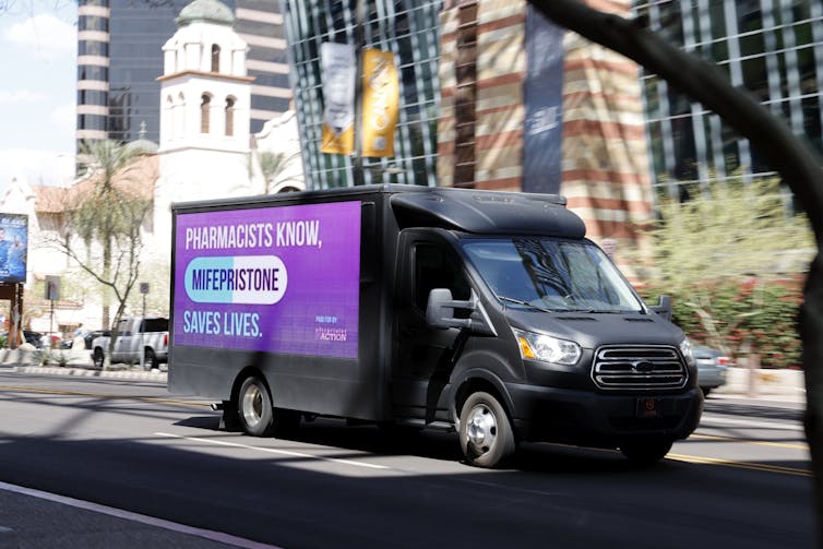 A truck shows a purple advertisement on its side that says, 'Pharmacists know, mifepristone saves lives.'