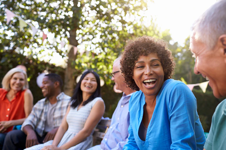 A woman in blue laughing in the foreground of a group of people sitting outside