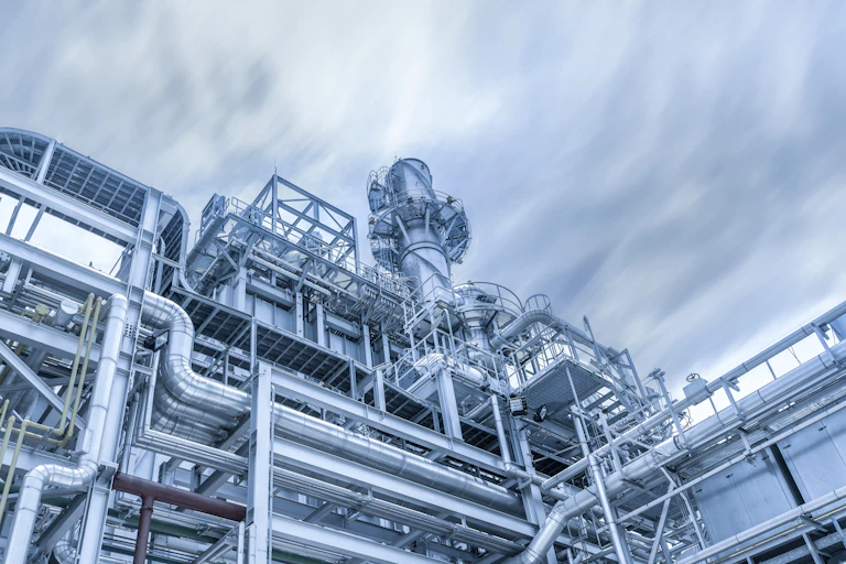 Silver tubes of a gas power plant with a gray sky with clouds.