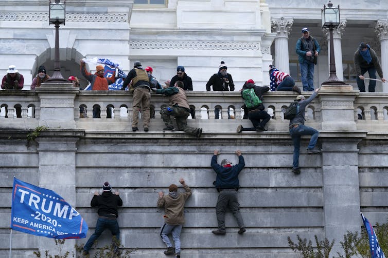 People climb a wall. A Trump flag waves behind them.