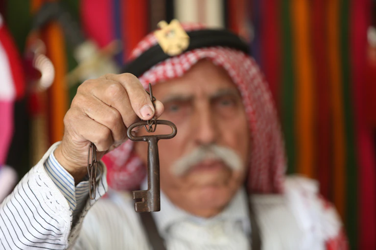 An Arab man holds up a large key.