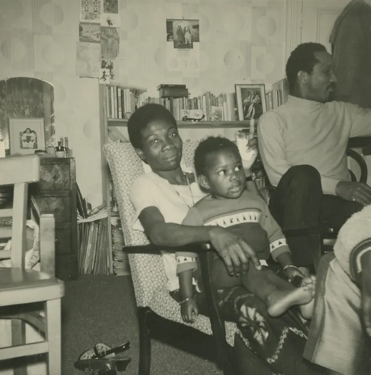 Jessica Huntley has daughter Accabre sat on her lap. Eric is to the right. They sit in a front room surrounded by books.