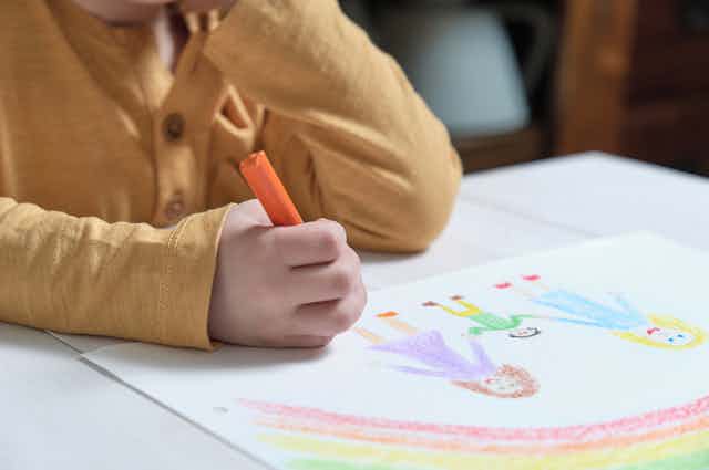Child drawing rainbow and family