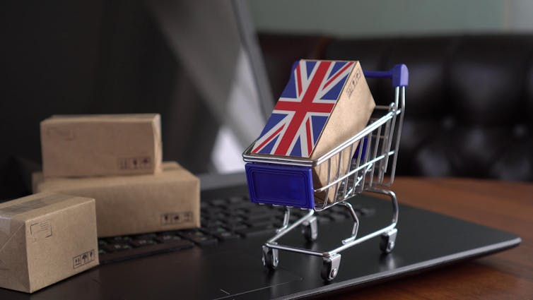 Parcel Boxes with a flag of United Kingdom in a mini shopping cart on a laptop.