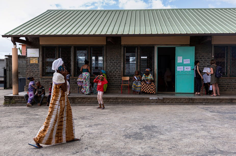Une femme passe devant des personnes qui attendent dehors lors d'une réunion entre des personnes menacées d'expulsion et des associations, dans le cadre d'une éventuelle procédure de relogement, à l'école élémentaire de Majicavo Dubaï, à Majicavo, Mayotte, le 24 avril 2023.