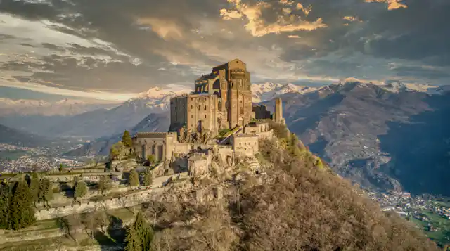 An ancient monastery on top of a hill in front of a mountain range.