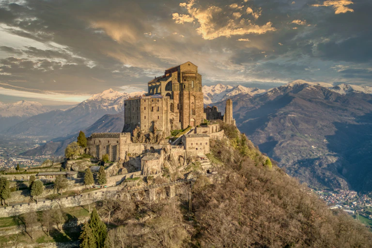 An ancient monastery on top of a hill in front of a mountain range.