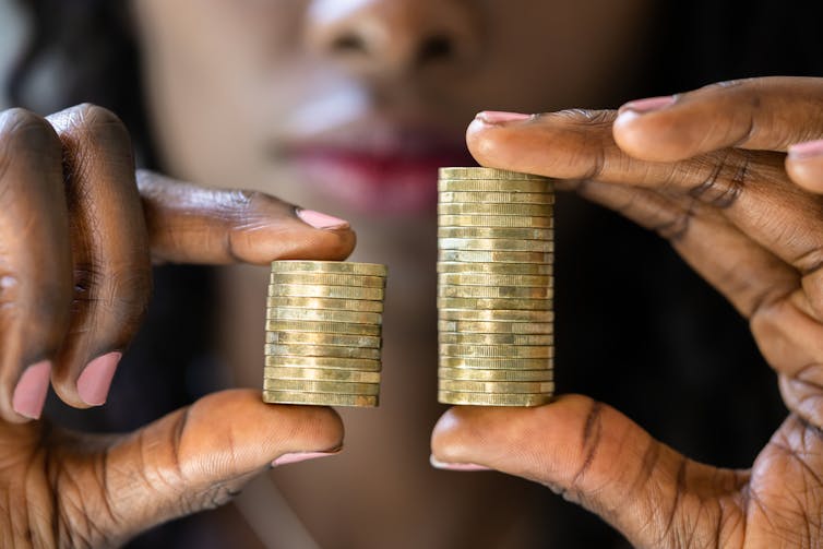 Woman holding larger stack of coins in right hand than in left hand.