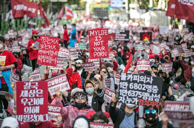 South Korean people marching holding red and black signs.