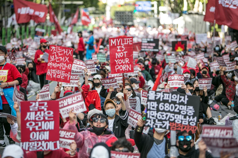 South Korean people marching holding red and black signs.