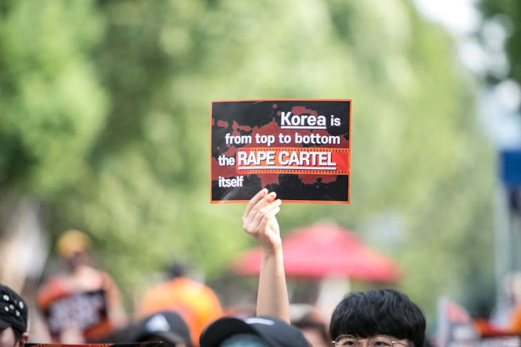 Protester holds sign that reads 'Korea is from top to bottom the rape cartel itself.'