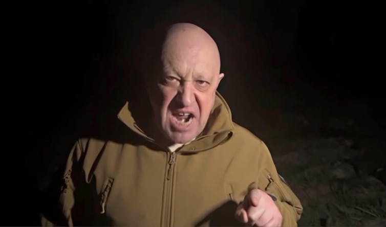Yevgeny Prigozhin, a bald man in a khaki, military coat gestures and yells angrily at the camera