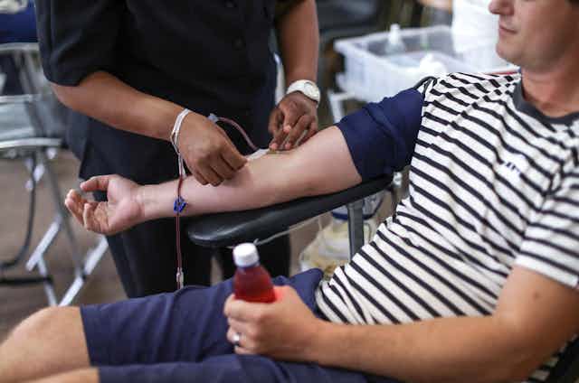 A man in a striped shirt has his arm extended while a technician extracts blood through a tube.