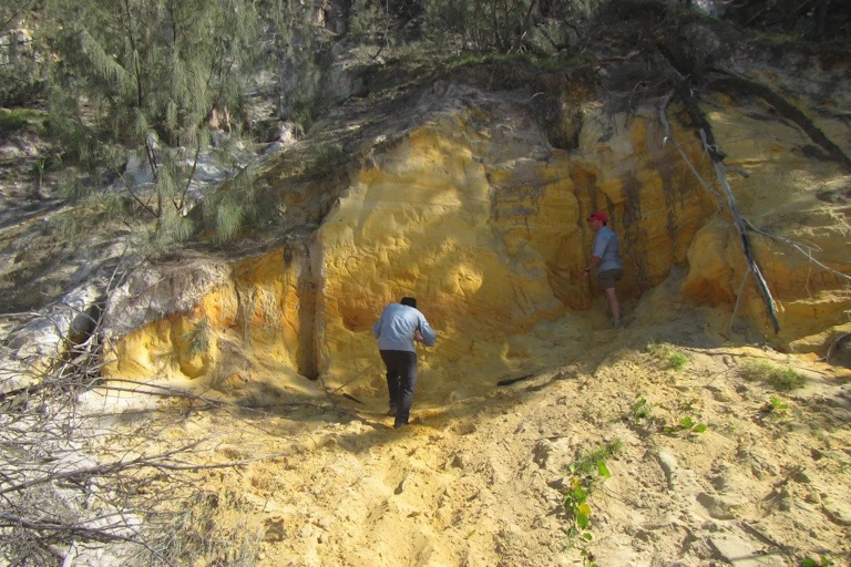 Two men stand at the foot of an excavation into a large sand dune