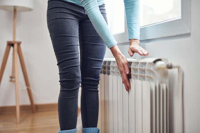 women warms hands on a radiator inside house