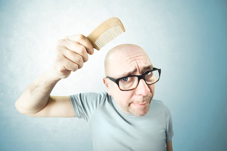 A bald man combs his head.