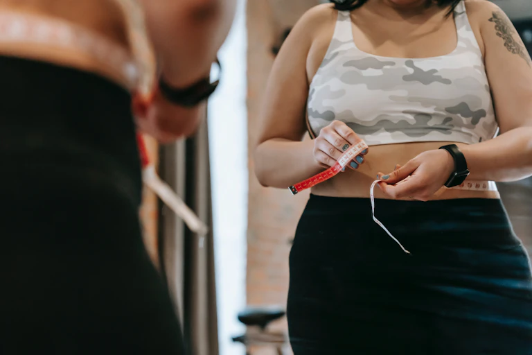 woman looks in mirror with measuring tape around waist