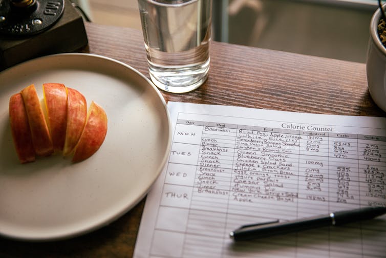 Apfelscheiben auf einem Teller neben der Liste der verzehrten Lebensmittel und Kalorien