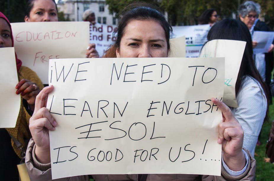 A woman holds up a sign saying WE NEED TO LEARN ENGLISH ESOL IS GOOD FOR US!